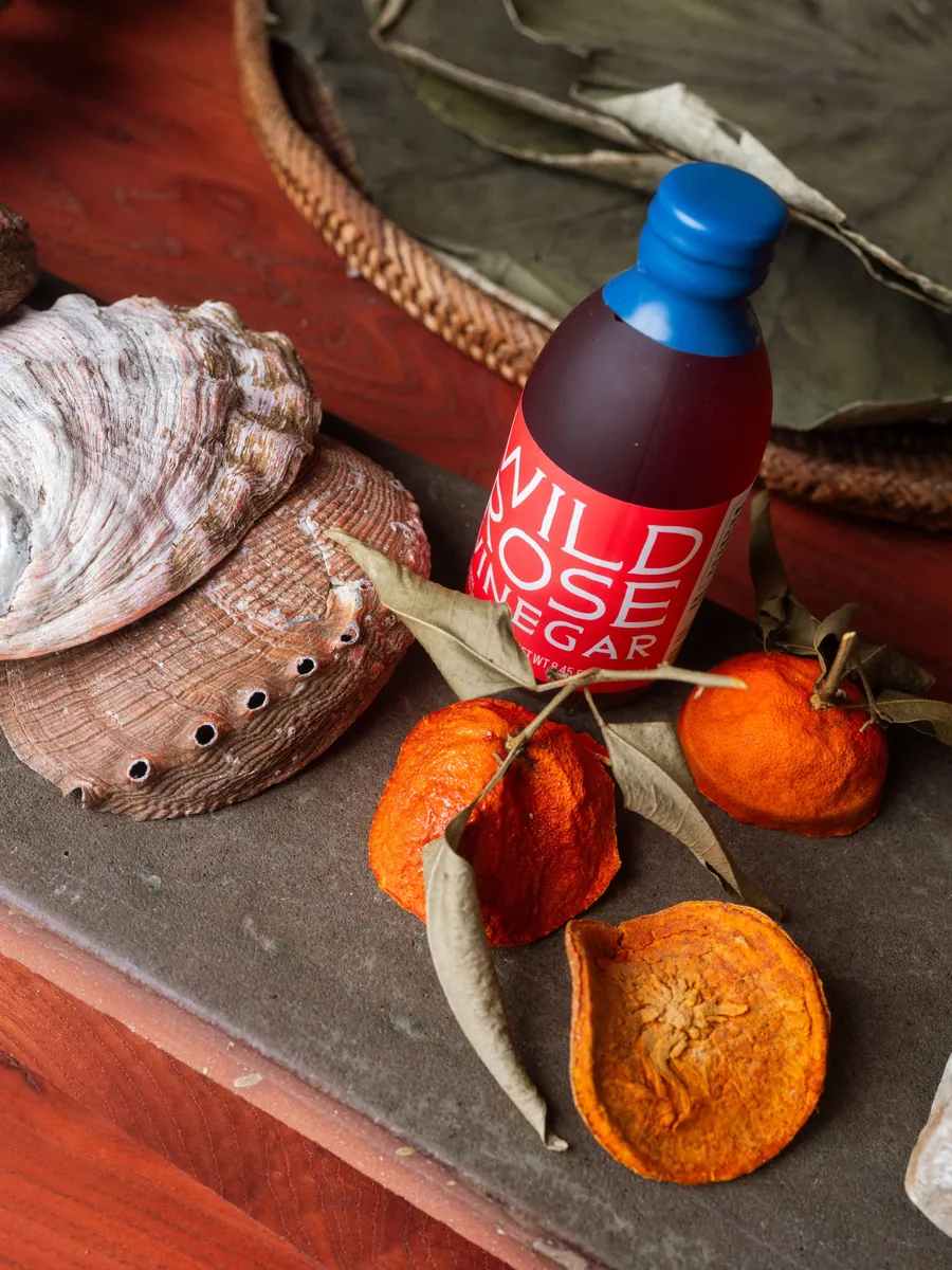 Eine Flasche Wild Rose Vinegar von Noma Projects mit getrockneten Mandarinen und einer Muschel